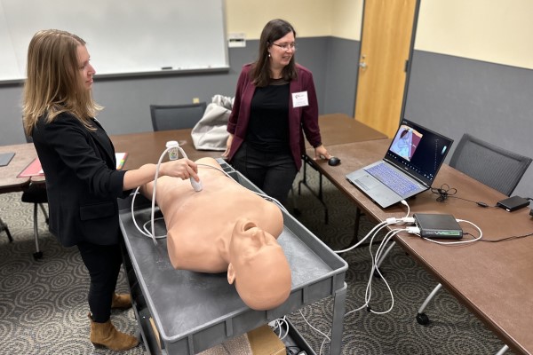 Two women practice using medical equipment on a medical mannequin.
